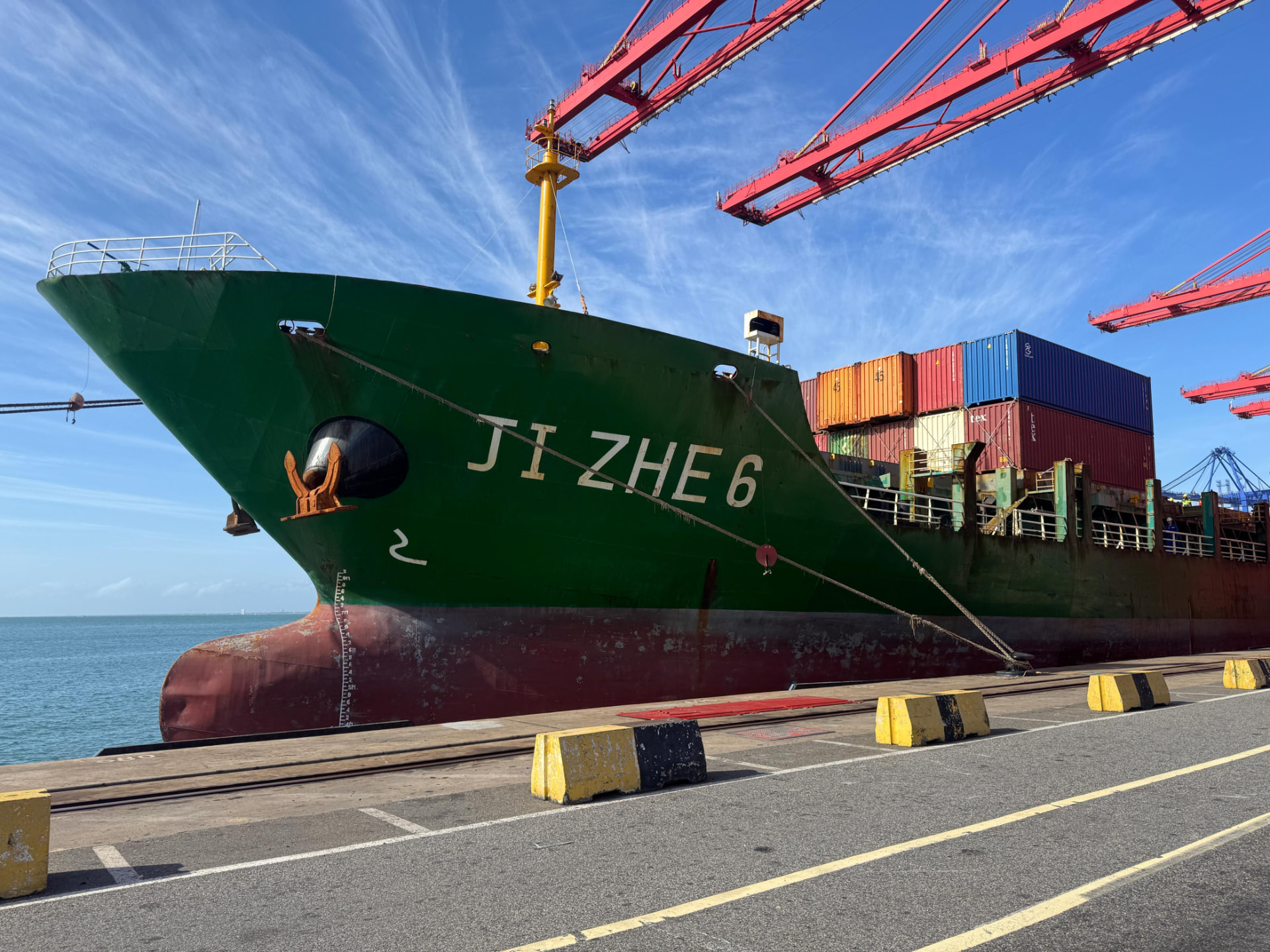 Container vessel JI ZHE 6 berthed alongside the quay under red gantry cranes