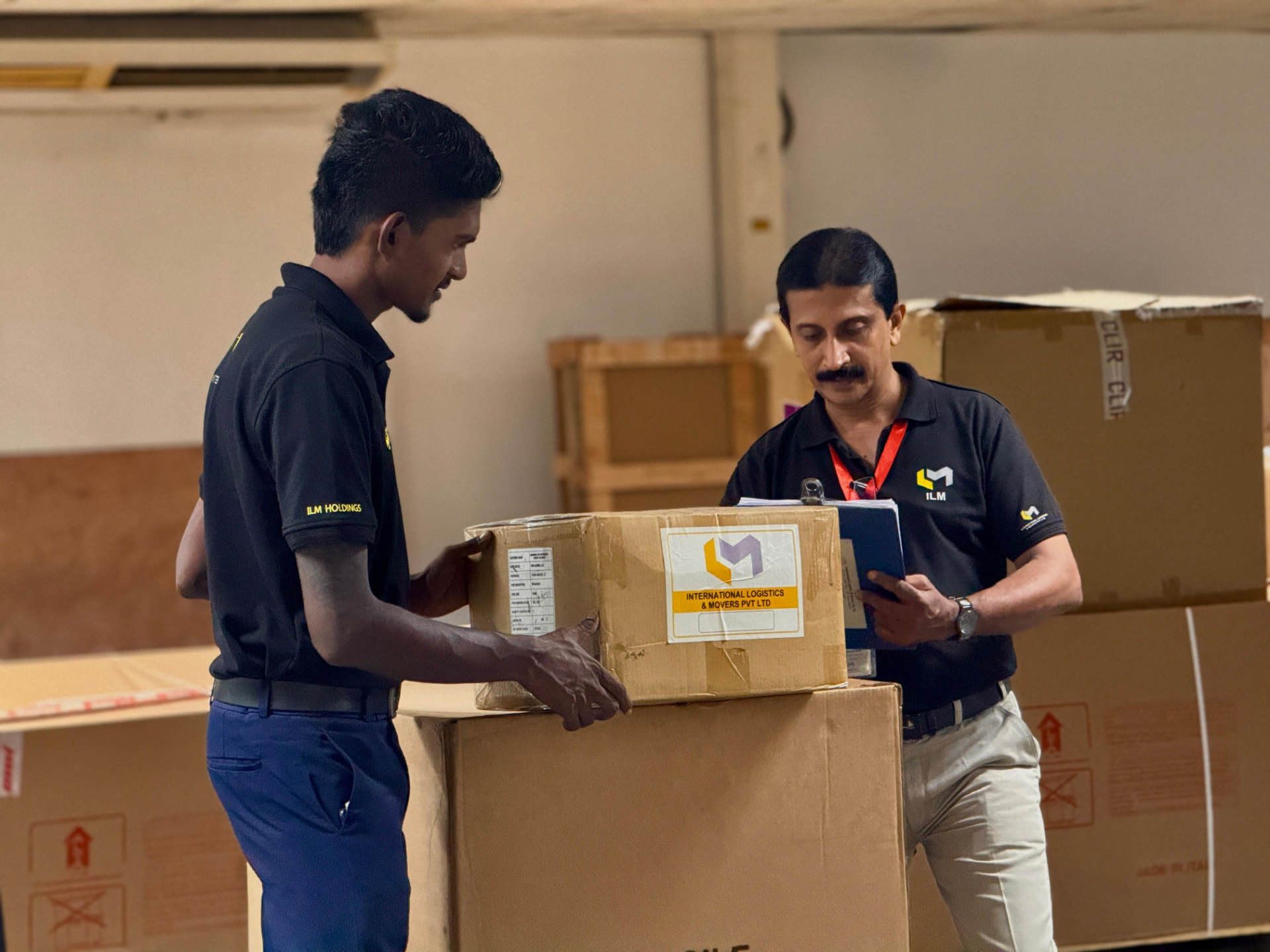 Two International Logistics & Movers staff checking a cartoned shipment in the warehouse