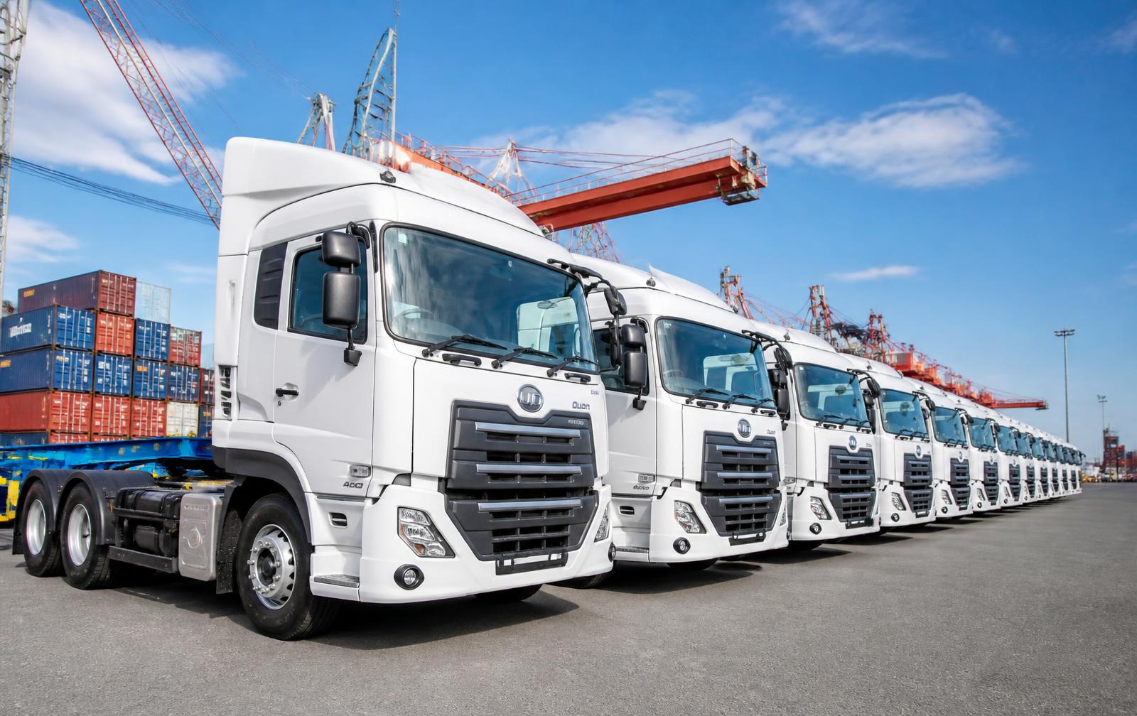 Row of new white prime mover trucks lined up in a container port yard
