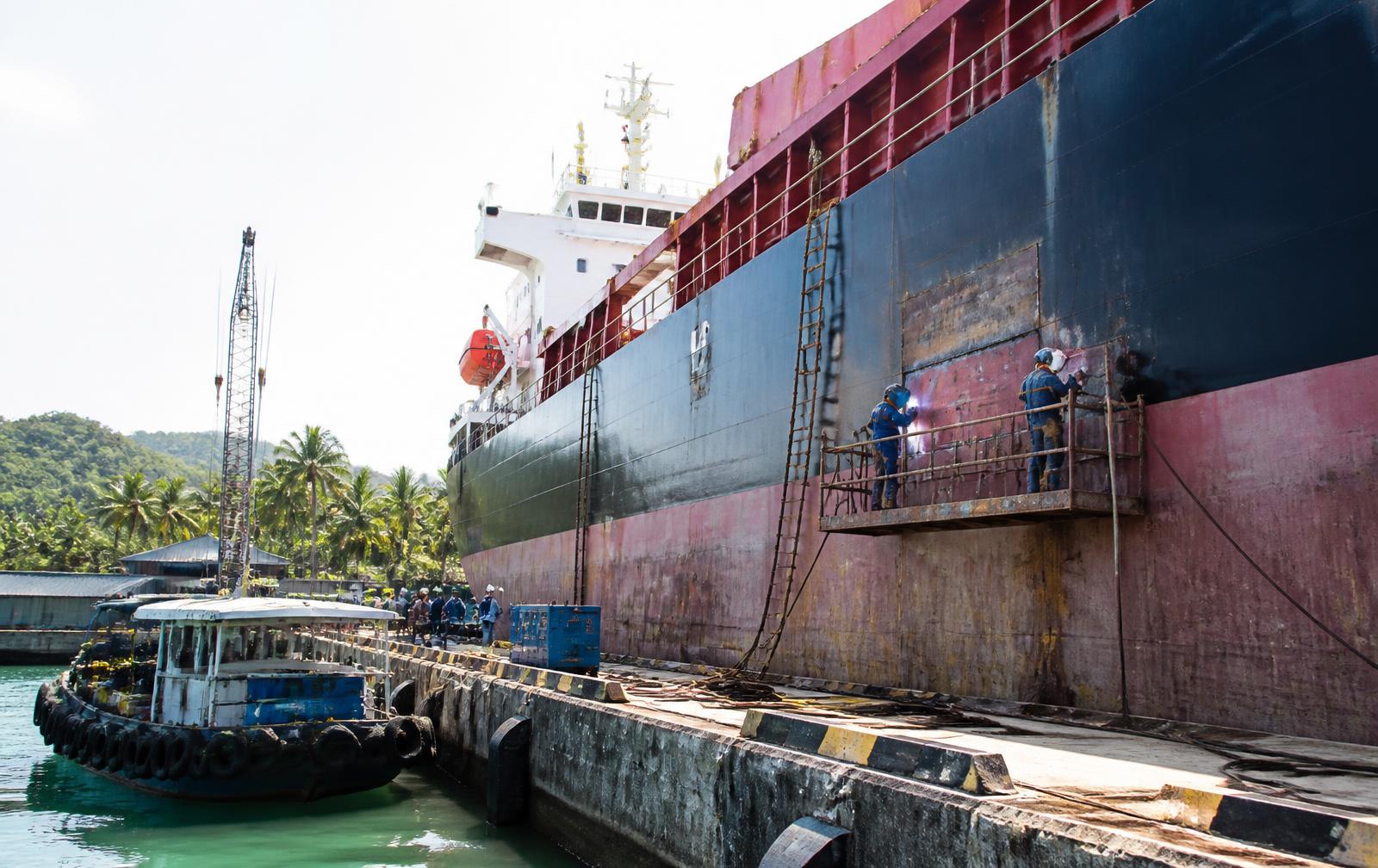 Cargo vessel undergoing hull repair alongside a tropical port quay